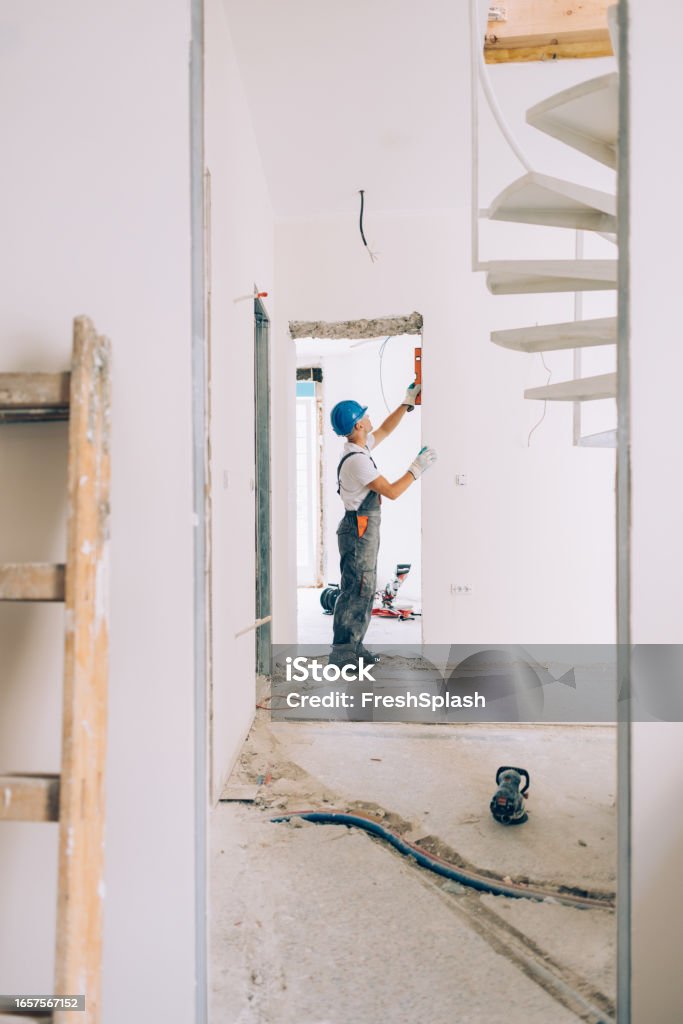 Trabajador de la construcción caucásico revisando las medidas de nivel dentro de un apartamento - Foto de stock de Solar de construcción libre de derechos